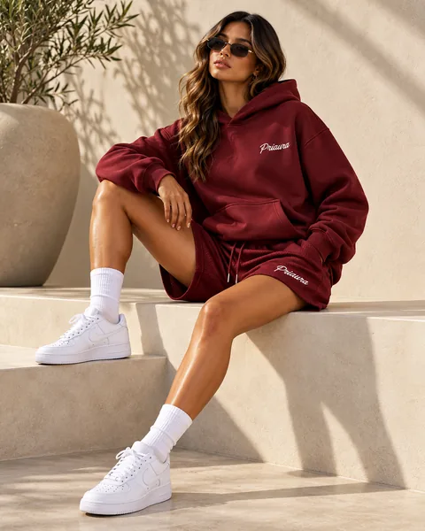 A model seated in sunlight in the Burgundy hoodie and mesh shorts