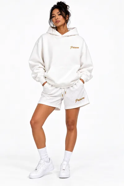 A model in the White holiday hoodie and mesh shorts with the gold Priaura script